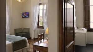 A bedroom with a bed, a chair, a table, a TV, and a window with curtains.
