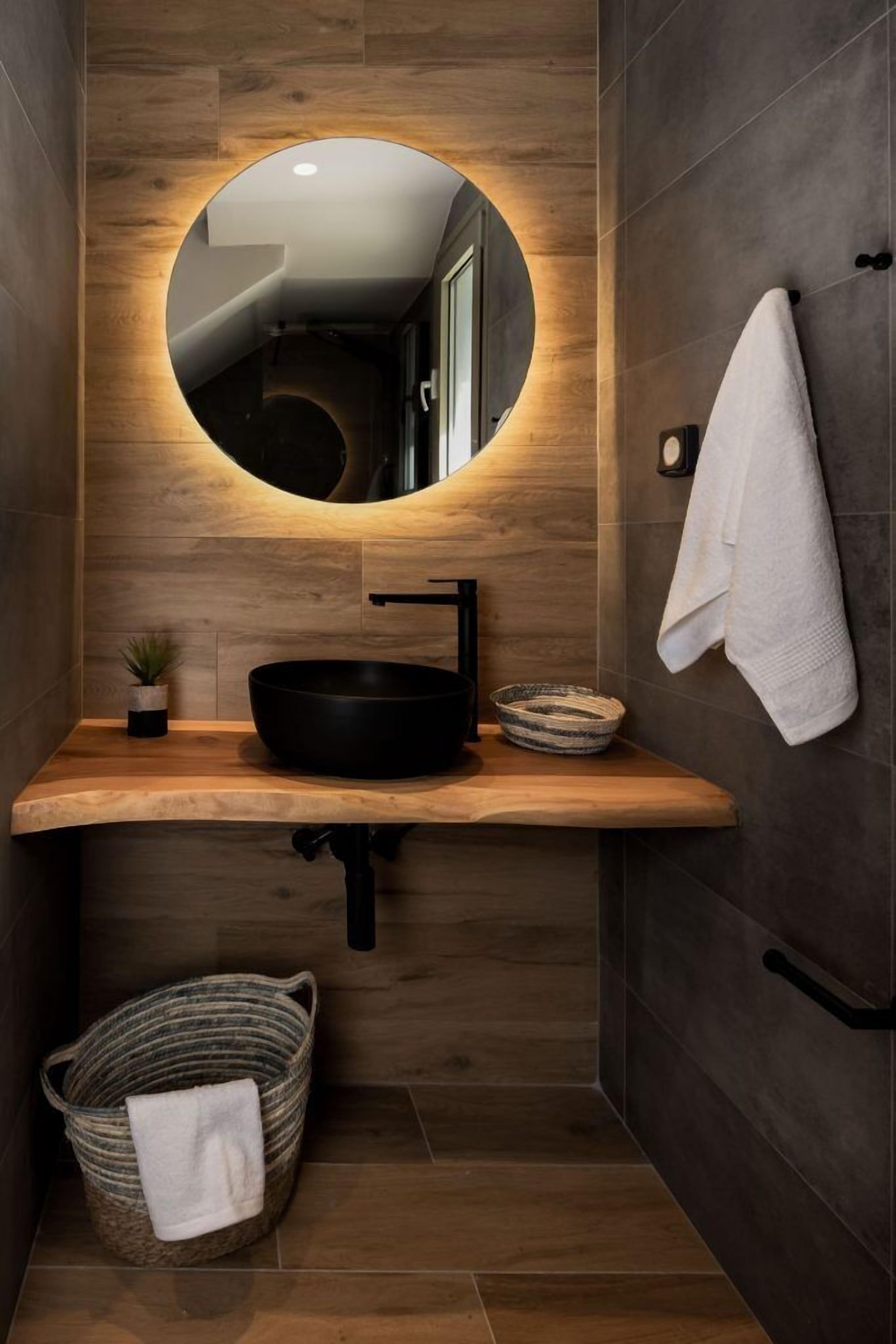 Une salle de bain moderne avec un meuble-lavabo en bois, un miroir rond, un lavabo noir et un porte-serviettes.