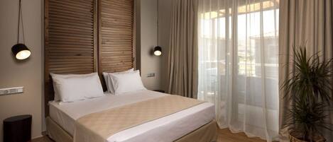 A bedroom with a large bed, wooden headboard, two bedside lamps, a potted plant, and sheer curtains.