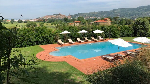 Ein Pool mit Liegestühlen und Sonnenschirmen, umgeben von Grünflächen und Blick auf entfernte Gebäude.