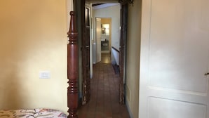 Ein schmaler Flur mit einem Bett links, einer Tür rechts und einer Treppe, die zu einer oberen Etage führt.