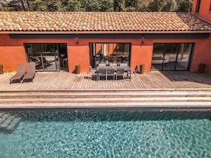 Un espace aménagé au bord de la piscine, avec une terrasse en bois, des chaises longues et une table entourée de chaises.