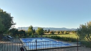 A rectangular swimming pool surrounded by a metal fence, with a clear view of distant hills and a grassy field.