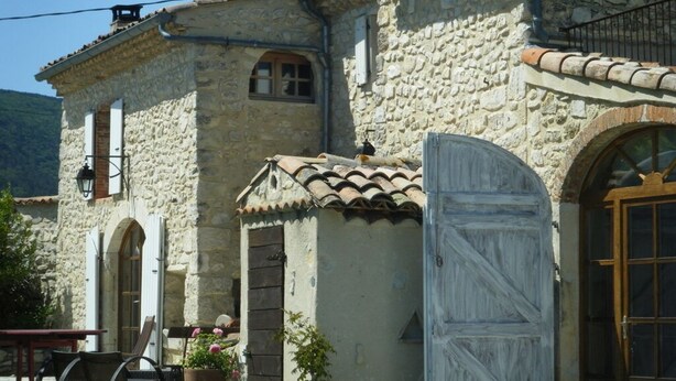 A stone building with a tiled roof, a wooden door, and a window with shutters.