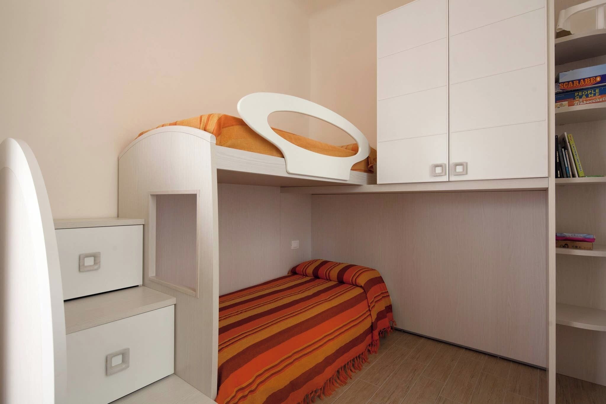 Ein Etagenbett mit Oberschrank, ein Nachttisch und eine kleine Ablage mit Büchern.