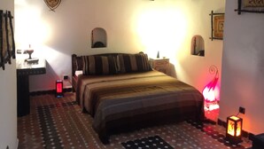 A bedroom with a bed, a nightstand, a wall-mounted shelf, and a patterned floor. - Riad Bab Essaouira (Essaouira)