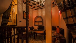A cozy room with a patterned floor, a round table, and a sofa. There is a decorative archway and a hanging light fixture. - Riad Bab Essaouira (Essaouira)