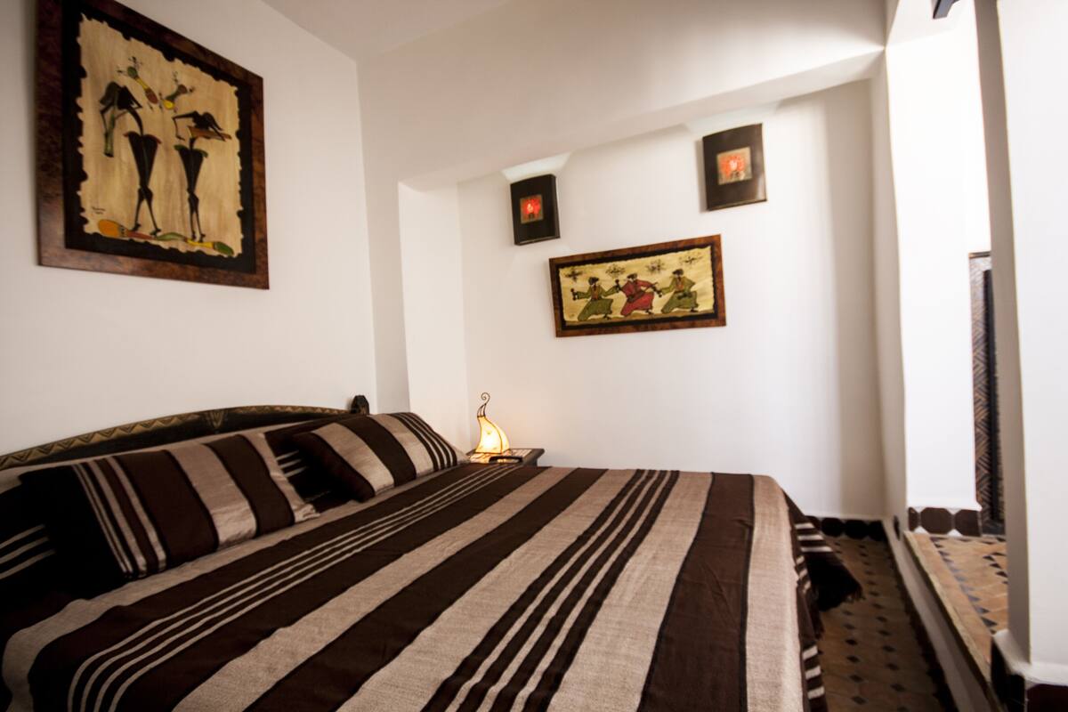 A hotel room with a large bed, a nightstand with a lamp, and wall art.