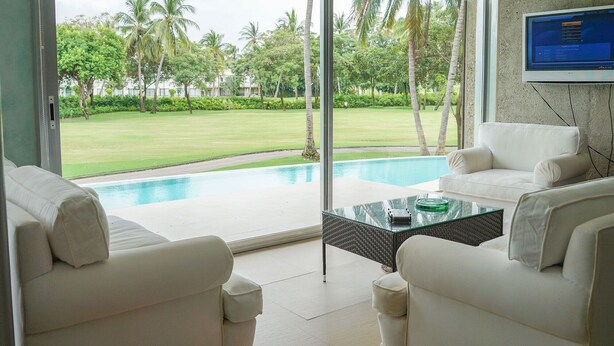 A modern living room with a pool view, white sofas, a glass coffee table, and a TV mounted on the wall. - Magnificent Loft in the Best Area of Acapulco (Acapulco)