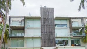 A modern multi-story building with a central vertical feature, balconies, and a pool area. - Magnificent Loft in the Best Area of Acapulco (Acapulco)