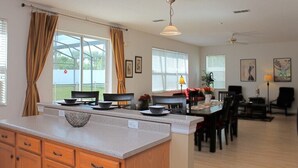 A spacious kitchen with a central island, large windows with curtains, and a dining area with chairs and a table. - Fl Special!! Berkeley Executive Pool 5 Bedroom Villa (Kissimmee)