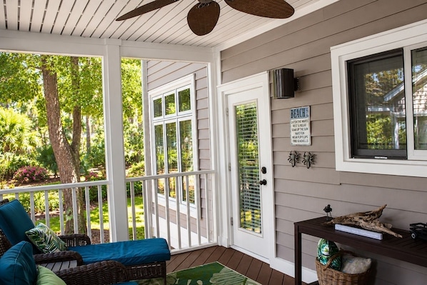 A covered porch with a wicker chair, a table with decorative items, and a sign about beach activities.