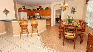 A spacious kitchen with wooden cabinets, a dining area with a chandelier, and a tiled floor. - 337 Belfry 6 Bedroom Villa by RedAwning (Davenport)