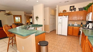 A compact kitchen with wooden cabinets, a central island, and a refrigerator. - 337 Belfry 6 Bedroom Villa by RedAwning (Davenport)