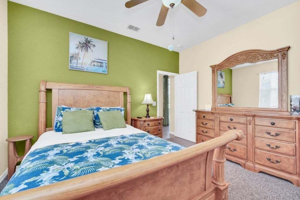 A bedroom with a wooden bed, green walls, a ceiling fan, a dresser, and a mirror.
