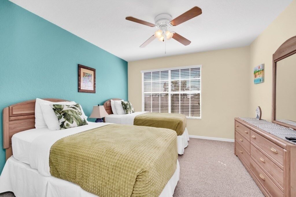 A bedroom with two beds, a ceiling fan, a window with blinds, a dresser, and a framed picture on the wall.