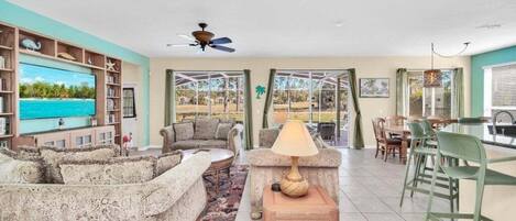 A spacious living room with a television, sofas, a coffee table, and a dining area with chairs and a table.