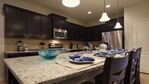 A kitchen with dark cabinets, stainless steel appliances, a granite countertop, and blue napkins on the island. - Windsor At Westside-2167amtjgi 8 Bedroom Home by RedAwning (Kissimmee)