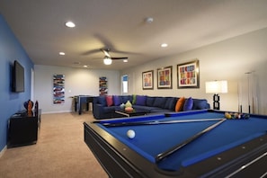 A pool table in a room with a blue couch, a ceiling fan, and artwork on the walls.