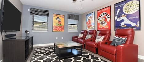 A living room with a flat-screen TV, a ceiling fan, a red leather sofa, a coffee table, and a patterned rug.
