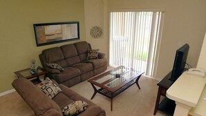 A living room with a brown sofa, a glass coffee table, and a television on a stand. - Regal Palms Resort 4 Bedroom Townhome! Townhouse by RedAwning (Davenport)