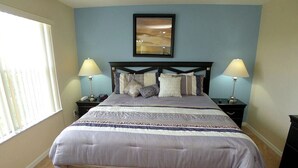 A bedroom with a bed, two bedside tables, a nightstand, a lamp, a framed picture on the wall, and a window with blinds. - Regal Palms Resort 4 Bedroom Townhome! Townhouse by RedAwning (Davenport)