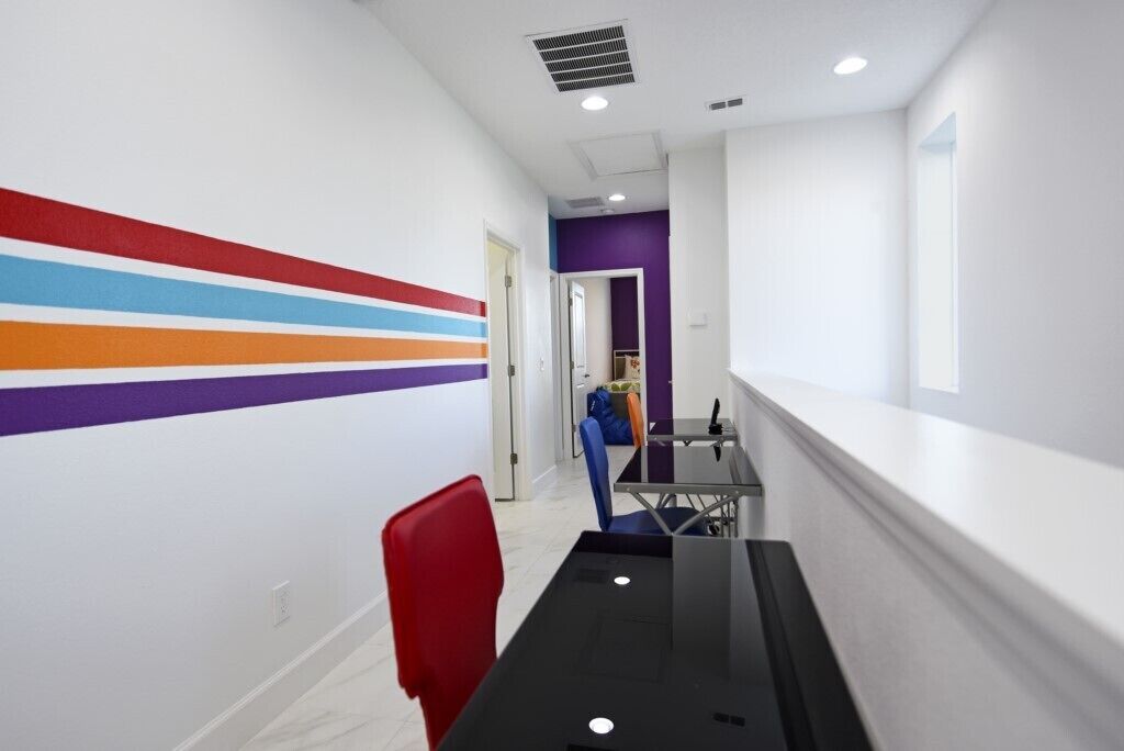 Un pasillo con una pared colorida, una mesa negra y una silla roja.