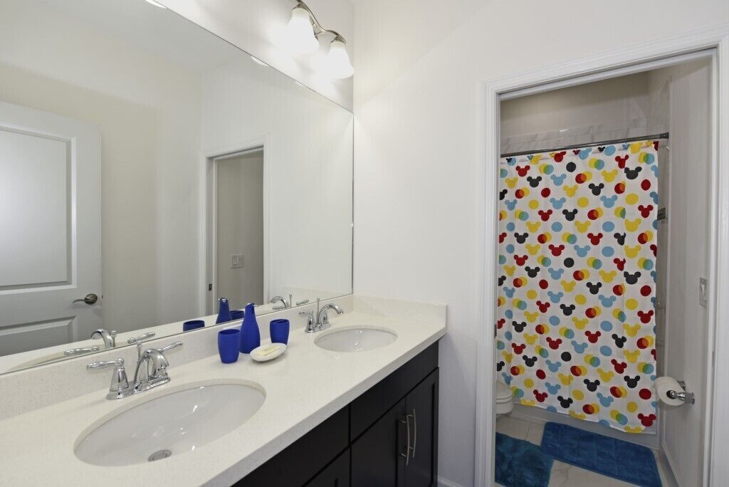 A bathroom with two sinks, a large mirror, and a Mickey Mouse themed shower curtain.