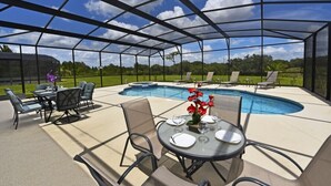 Un espace extérieur abrité comprenant une piscine, des sièges et une table dressée pour les repas.