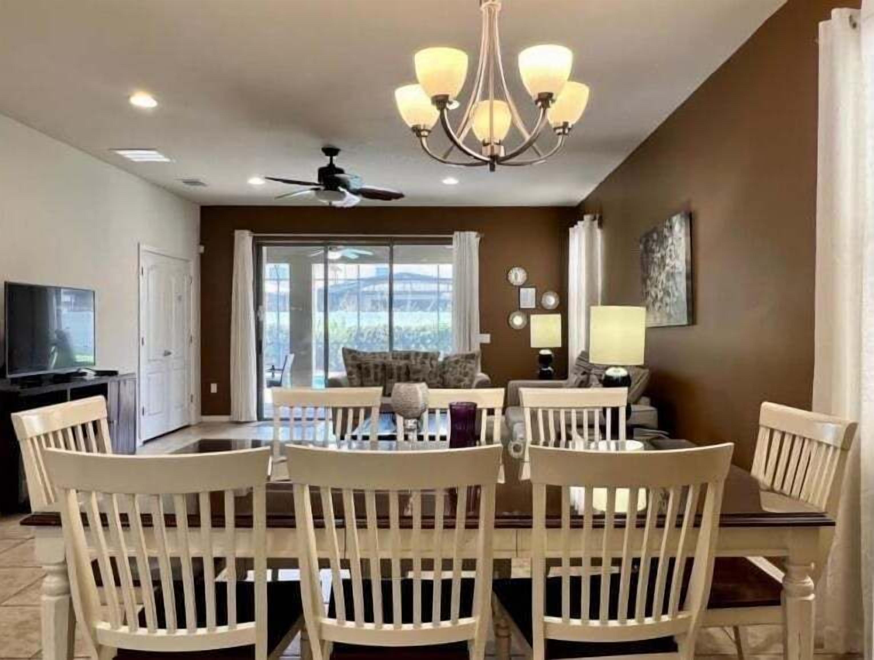 A dining area with a chandelier, a ceiling fan, and a television in the background.