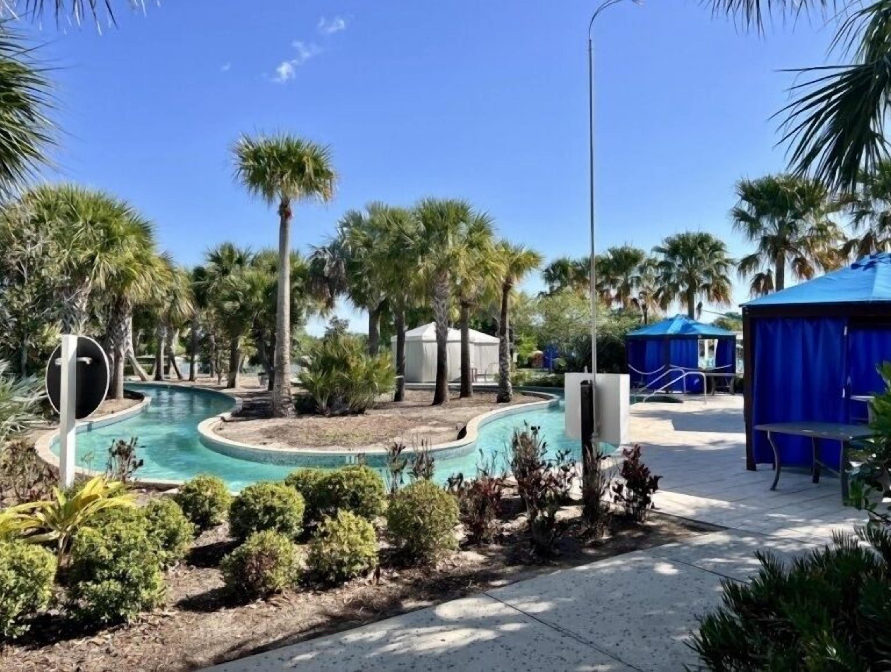 A pool area with palm trees, a blue tent, and a covered seating area.