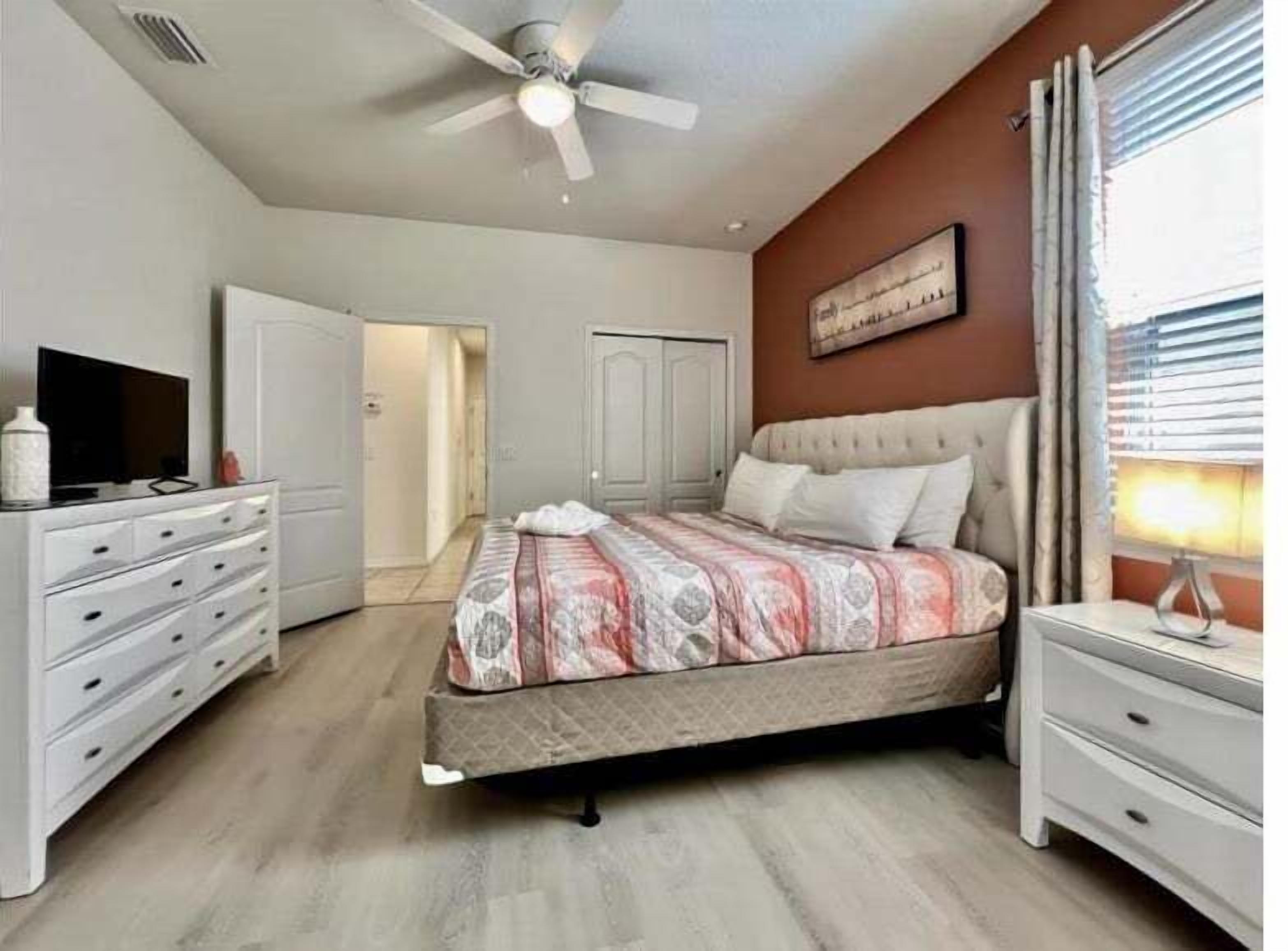 A bedroom with a bed, a dresser, a television, and a ceiling fan.