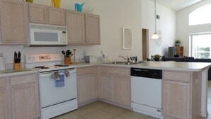 A modern kitchen with light wood cabinets, a white microwave, stove, and dishwasher. - Tm148or 4 Bedroom Home by RedAwning (Davenport)