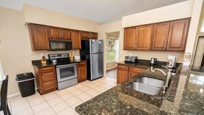 A kitchen with wooden cabinets, a stainless steel refrigerator, a microwave, a stove, and a granite countertop. - Wr001or 4 Bedroom Home by RedAwning (Davenport)