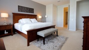A bedroom with a large bed, a wooden headboard, a bench, two bedside tables, and a fluffy rug. - Vista Cay Gem 3 Bedroom Condo by RedAwning (Orlando)