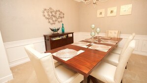 A dining room with a wooden table, white upholstered chairs, and a chandelier. - Vista Cay Gem 3 Bedroom Condo by RedAwning (Orlando)