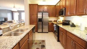A kitchen with wooden cabinets, a stainless steel refrigerator, a microwave, and granite countertops. - Vista Cay Dream 3 Bedroom Home by RedAwning (Orlando)