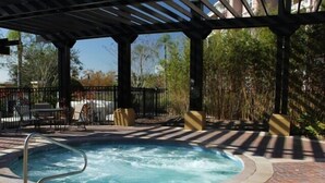 A hot tub under a covered area with a patio table and chairs, surrounded by a fence and greenery. - Vista Cay Dream 3 Bedroom Home by RedAwning (Orlando)