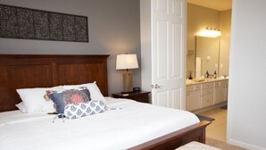 A neatly made bed with a wooden headboard, a bedside table with a lamp, and a large mirror in the adjacent bathroom. - Vista Cay Dream 3 Bedroom Home by RedAwning (Orlando)