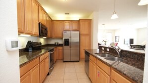 A kitchen with wooden cabinets, a stainless steel refrigerator, granite countertops, and a built-in dishwasher.