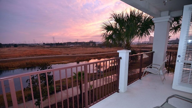 A balcony with a view of a marshy area and a sunset.