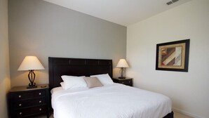 A neatly arranged bedroom with a large bed, two bedside tables with lamps, and a framed picture on the wall.