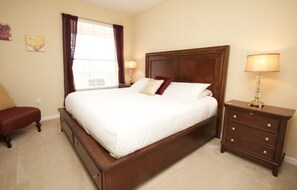 A bedroom with a large bed, a nightstand, a chair, and a window with curtains.