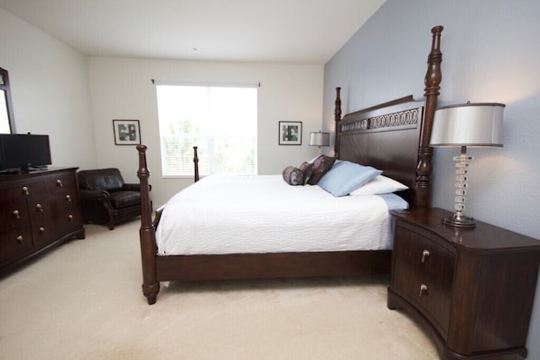 A bedroom with a large bed, dark wooden dresser, and a nightstand with a lamp.