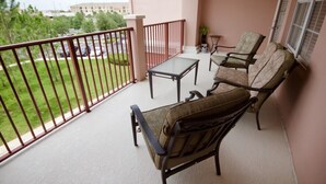 A balcony with a table and two chairs, a railing, and a view of a parking lot and greenery. - 7-301 3 Bedroom Condo by RedAwning (Orlando)