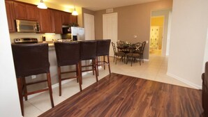 A kitchen with wooden cabinets, a microwave, and a dining area with a table and chairs. - 7-301 3 Bedroom Condo by RedAwning (Orlando)