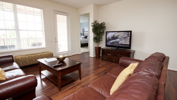 A living room with a brown leather sofa, a wooden coffee table, and a television on a stand. - 7-301 3 Bedroom Condo by RedAwning (Orlando)