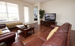 Een woonkamer met een bruine leren bank, een houten salontafel en een televisie op een dressoir.
