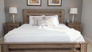 A bedroom with a wooden headboard, a white bedspread, two bedside tables with lamps, and two framed artworks on the wall. - Lakeview Fantasy New! 3 Bedroom Condo by RedAwning (Orlando)