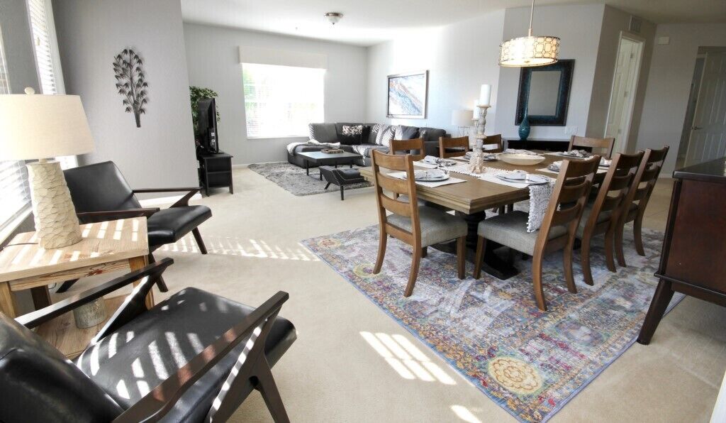 A dining area with a wooden table and chairs, a patterned rug, and a modern chandelier.